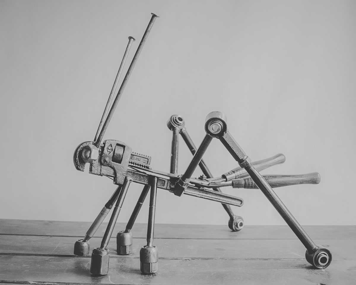 Handcrafted welded metal grasshopper sculpture made from industrial steel parts, displayed on a tabletop.