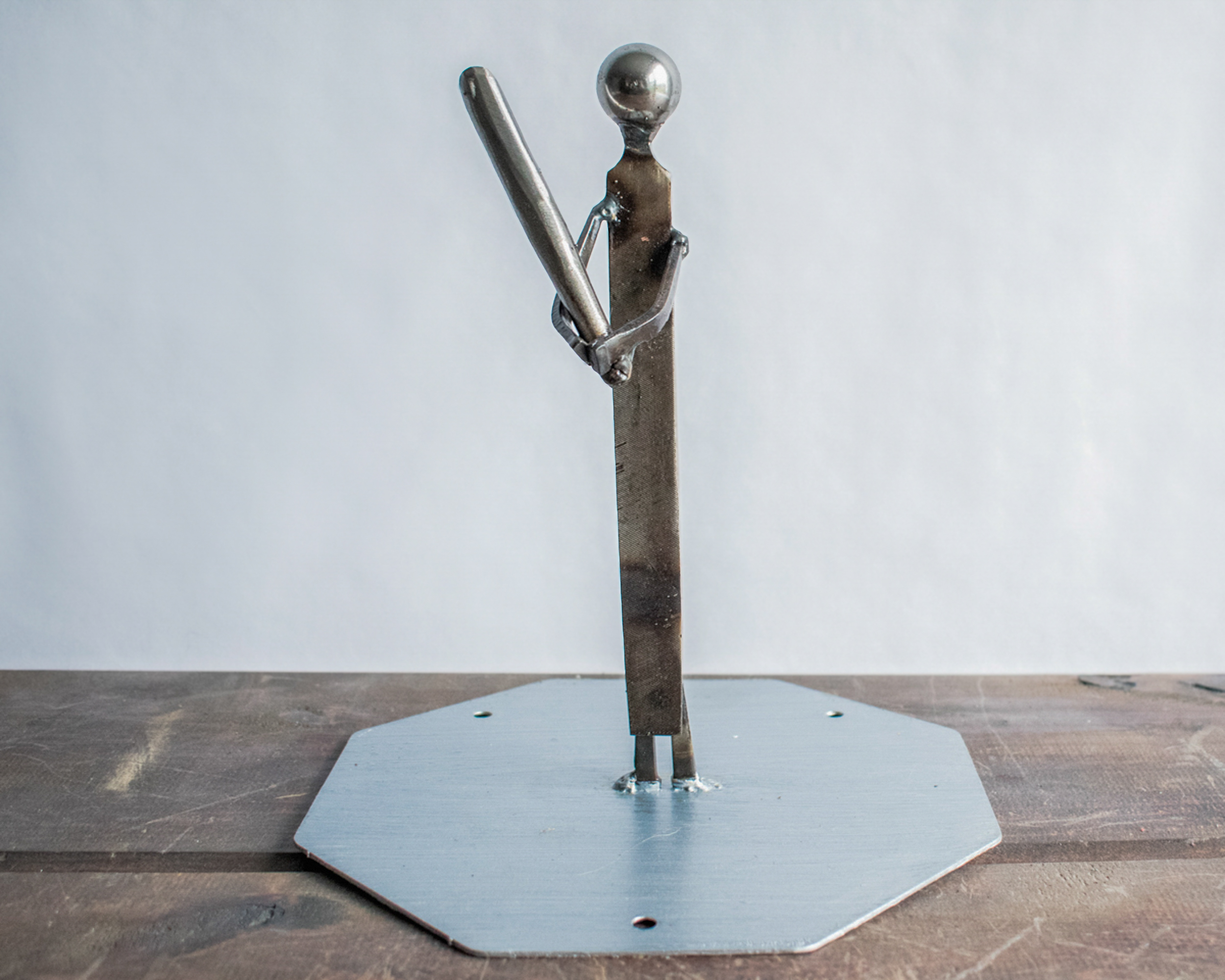 Handcrafted industrial metal baseball player sculpture capturing the quiet moment before the swing, made from reclaimed steel.