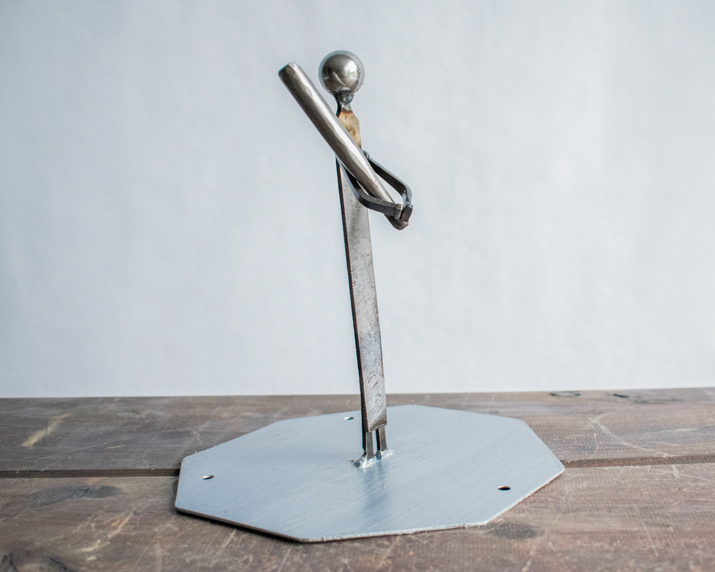 Side view of industrial metal baseball player sculpture with bat resting across the shoulder, showing relaxed yet powerful stance.