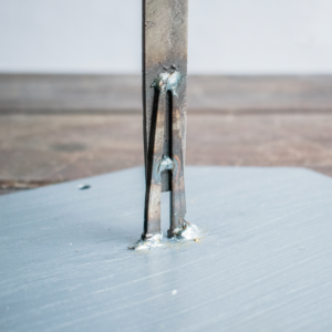 Close-up of the baseball player sculpture’s steel file body and square-head nail legs, showing raw texture and weld details.