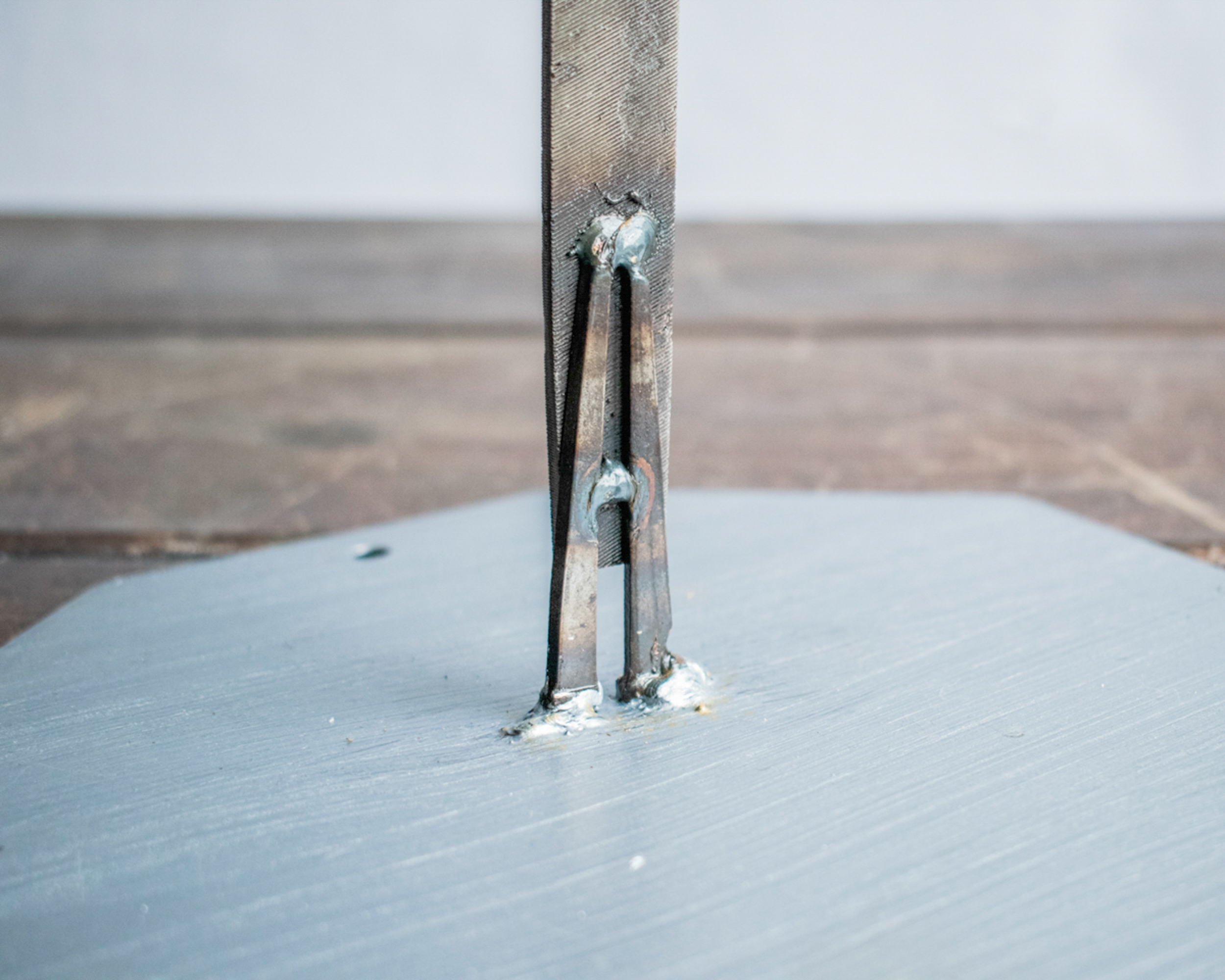 Close-up of the baseball player sculpture’s steel file body and square-head nail legs, showing raw texture and weld details.