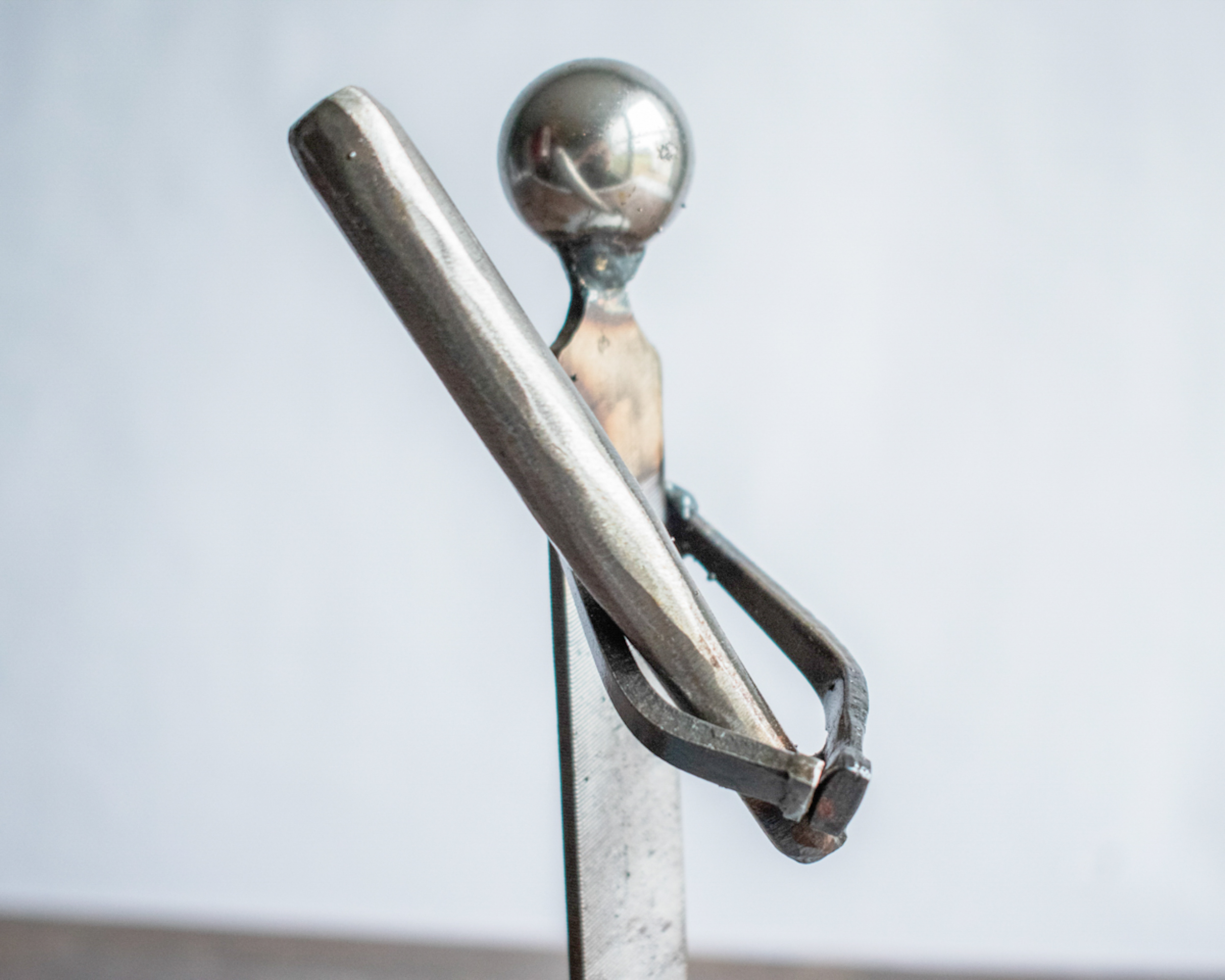 Close-up of the baseball bat and arm of the welded metal baseball player sculpture, emphasizing strength and precision.