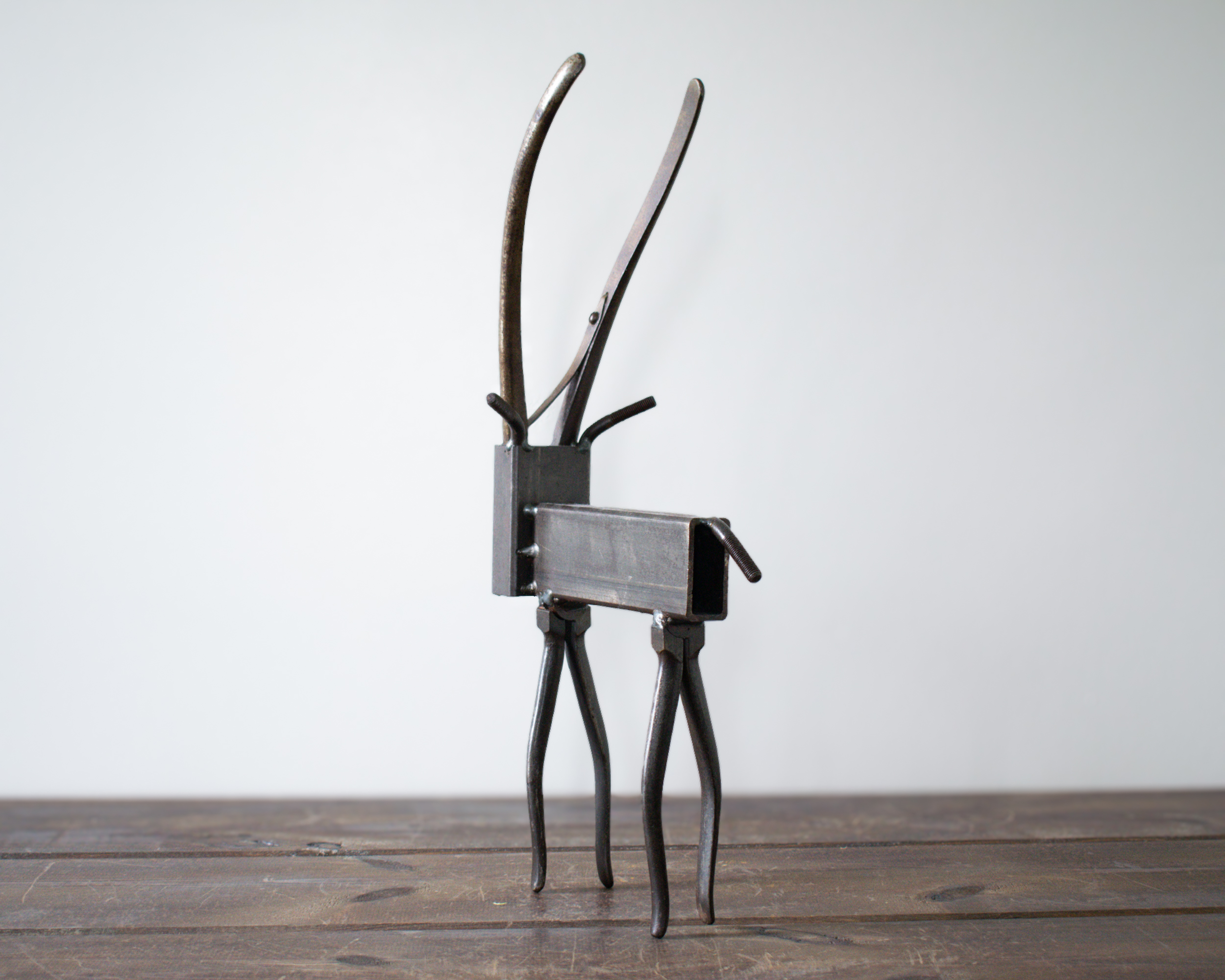 Rear view of welded metal antelope sculpture standing on four steel legs on wooden tabletop.