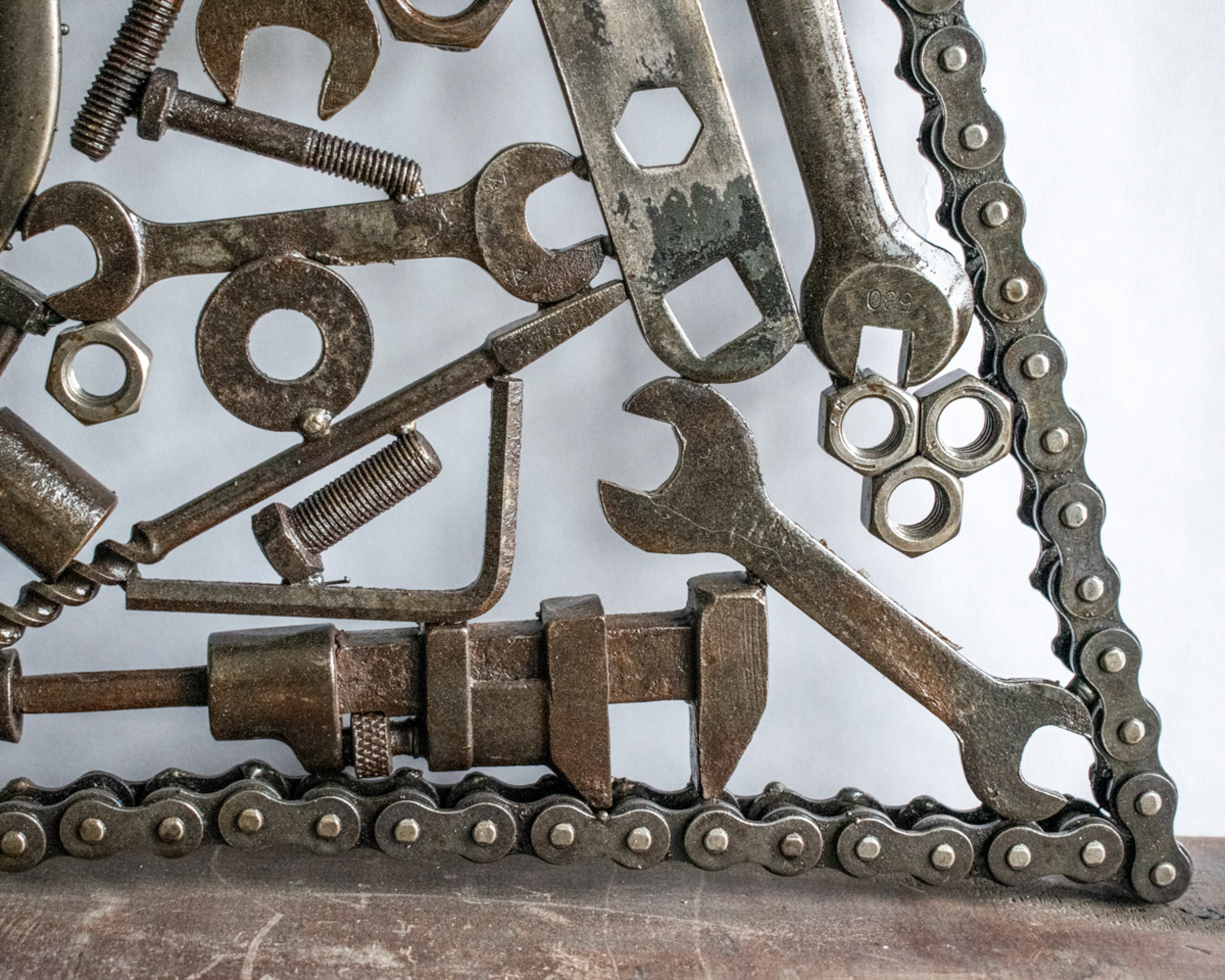 Lower portion of geometric welded metal wall art featuring bolts, wrenches, and reclaimed hardware
