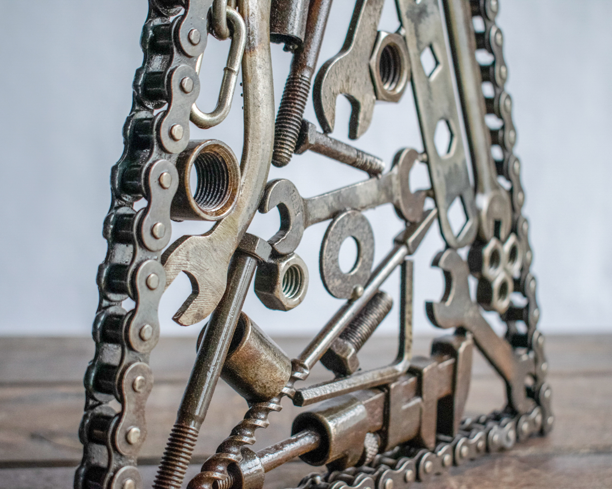 Angled side view of trapezium metal sculpture showing layered reclaimed tools welded inside a motorcycle chain frame