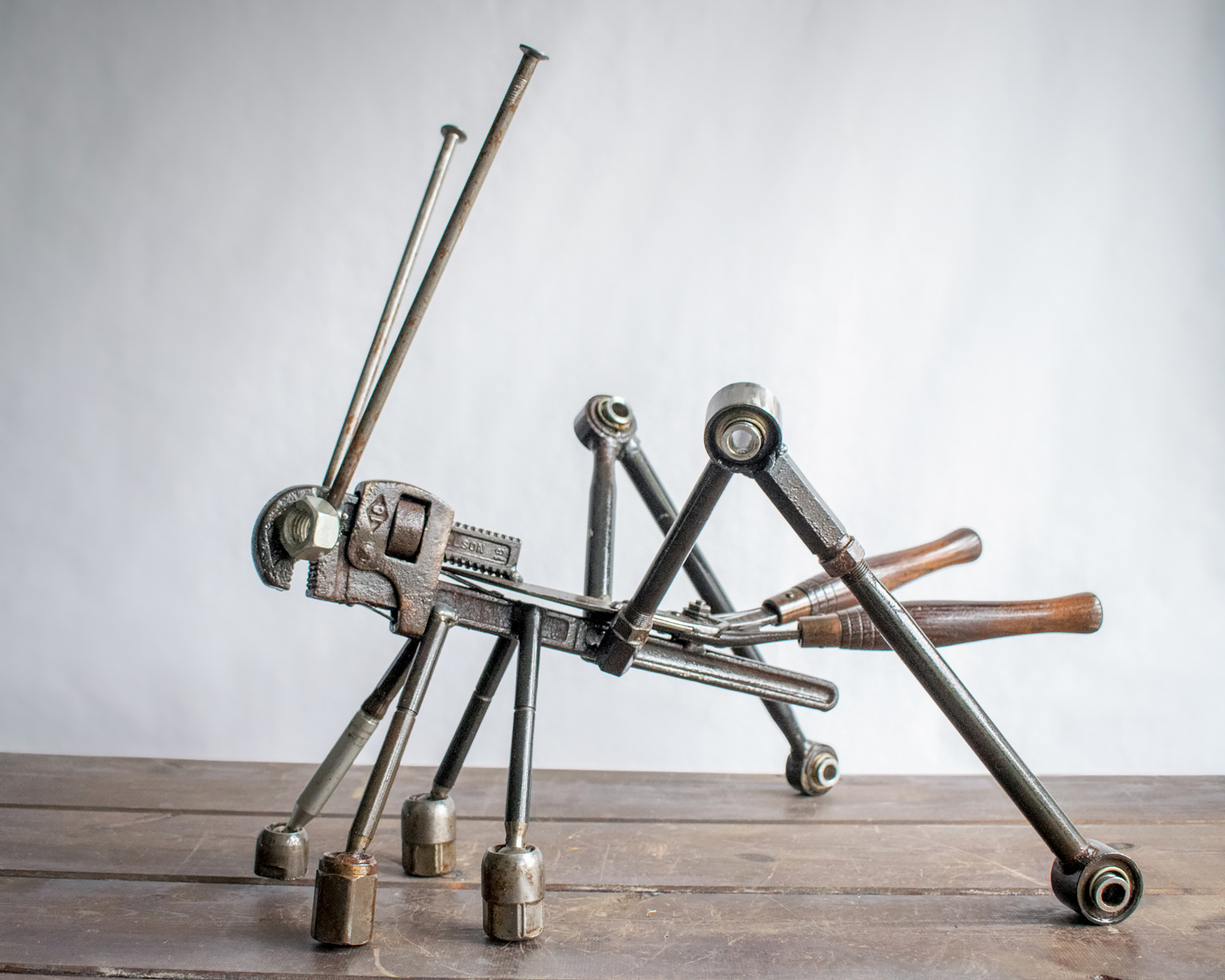 Metal grasshopper sculpture made from reclaimed steel, pipe wrench, shears, large nails, and car control arms.