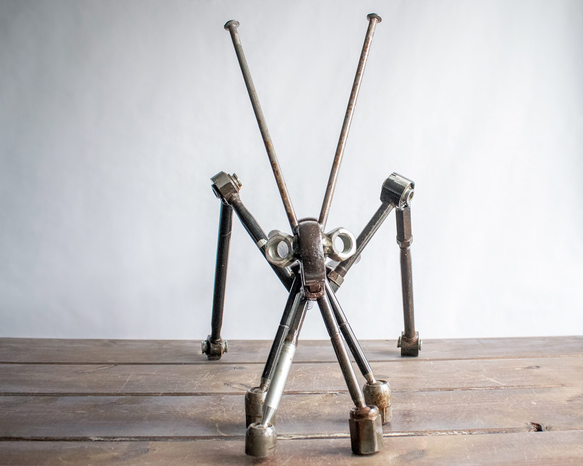Front view of industrial garden art shaped like a grasshopper with long metal legs and antennae.