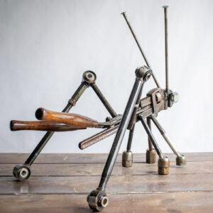 Angled view of reclaimed metal grasshopper sculpture with pipe wrench body and long steel legs.