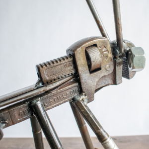 Close-up of pipe wrench body and welded leg details on a metal grasshopper sculpture.