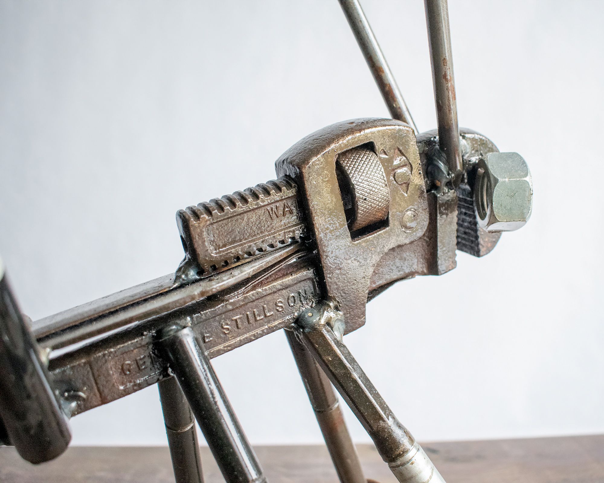 Close-up of pipe wrench body and welded leg details on a metal grasshopper sculpture.