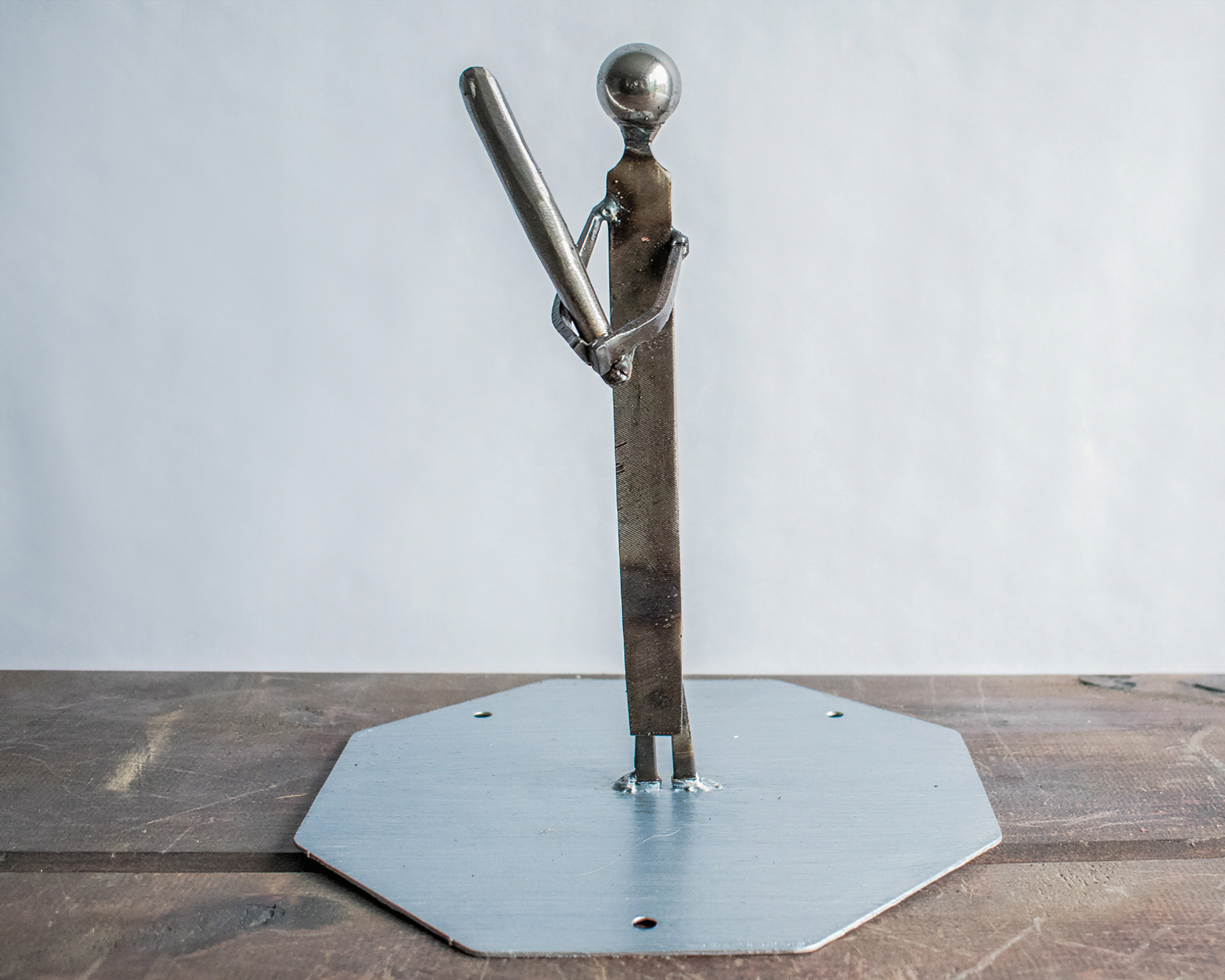 Metal baseball player sculpture made from a ball bearing, metal file, square-head nails, and steel base.