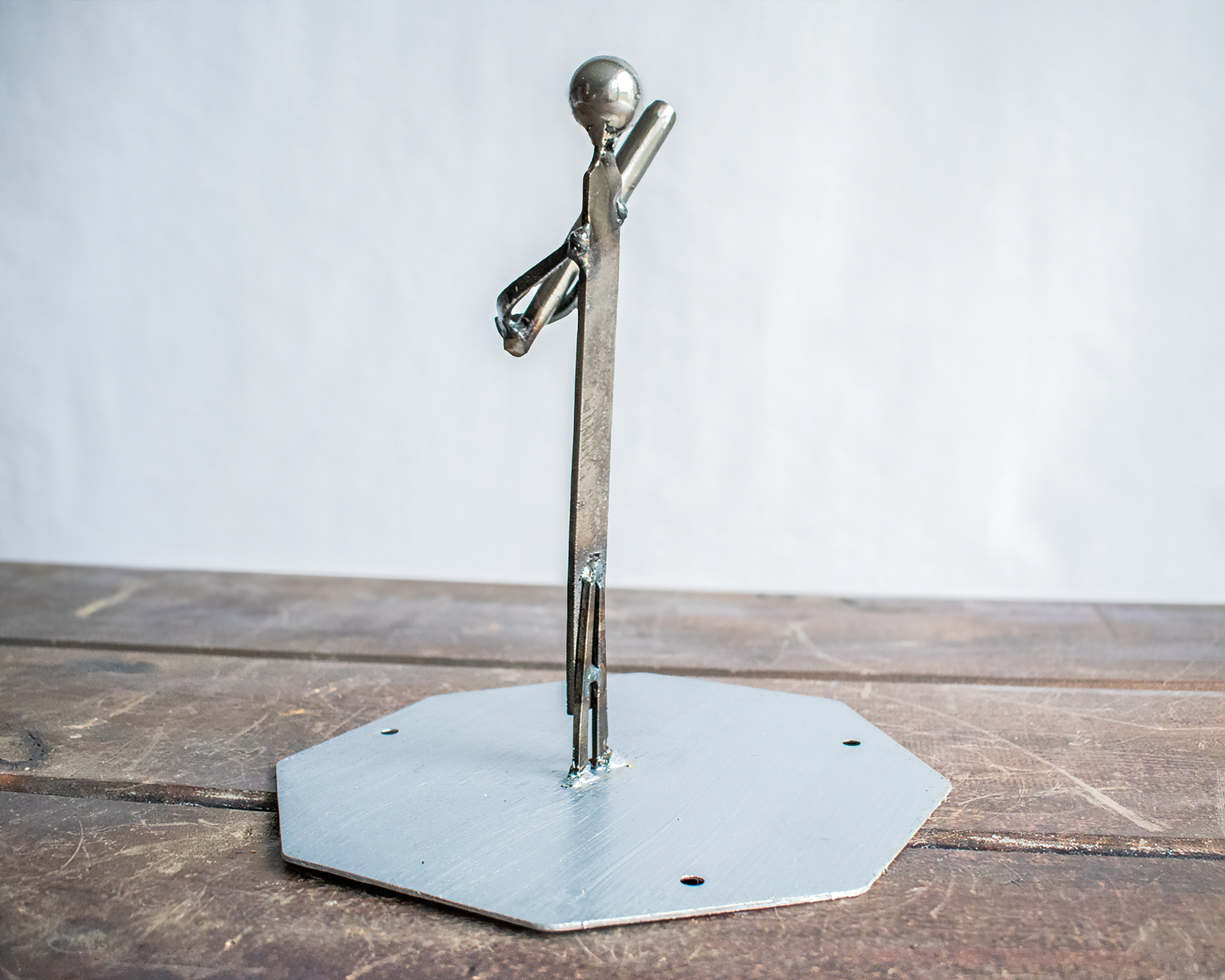 Angled view of a small metal baseball player sculpture on a steel tabletop base.