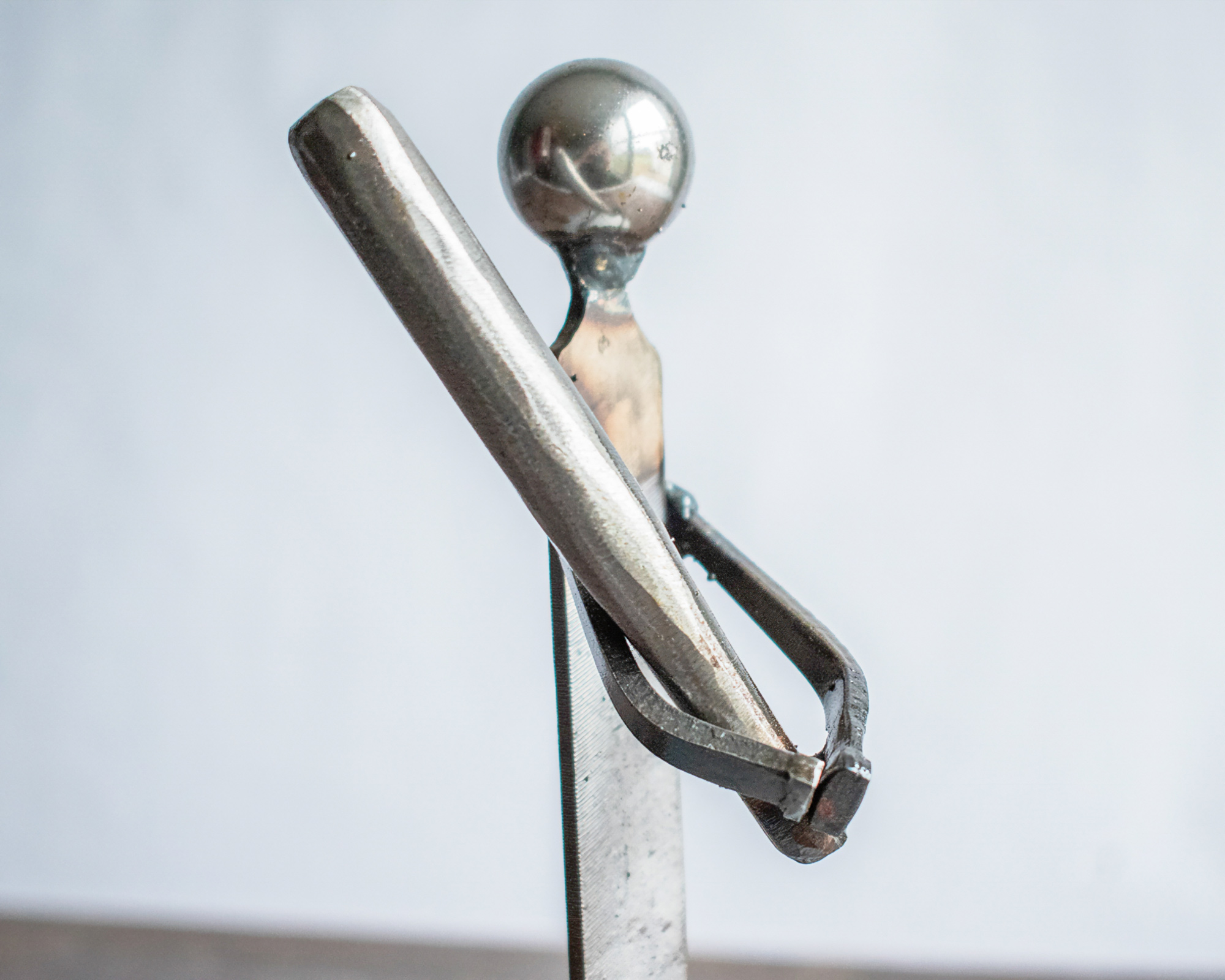 Close-up of the ball bearing head and metal bat on a metal baseball player sculpture.