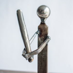 Close-up of welded arms, bat, and metal file body on a baseball player sculpture.