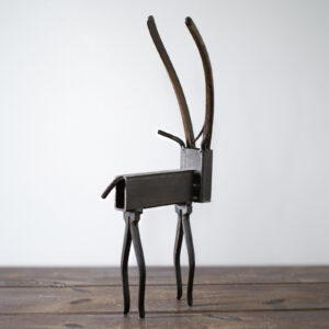 Angled view of reclaimed metal art shaped like a tall antelope with a raw steel finish.