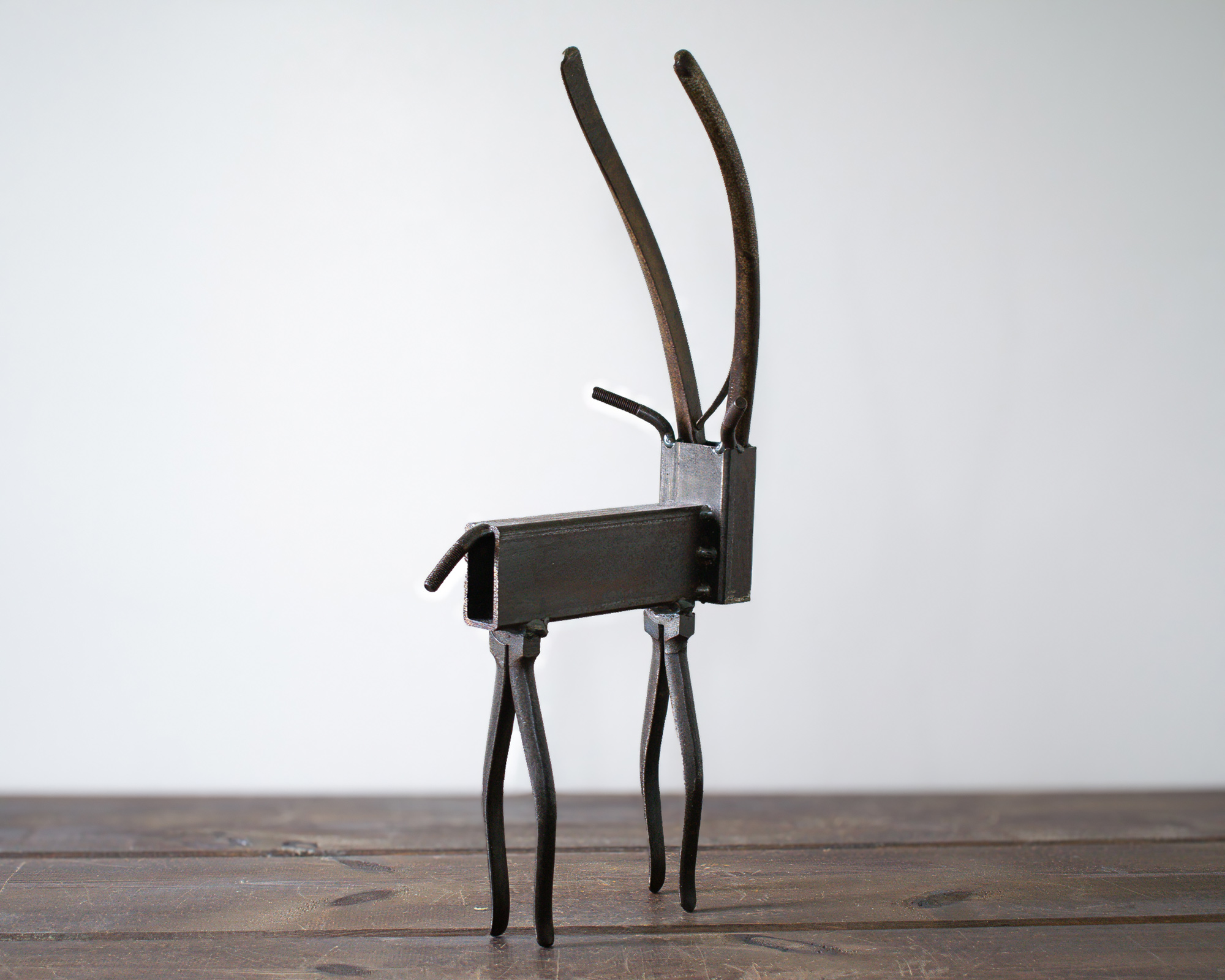 Angled view of reclaimed metal art shaped like a tall antelope with a raw steel finish.