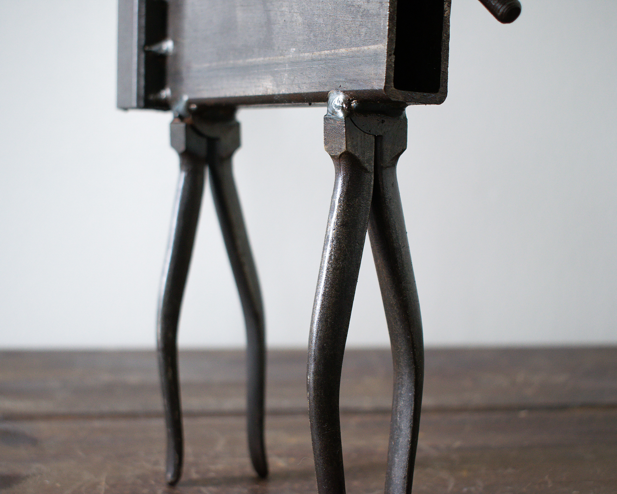 Close-up of the steel legs and welded body details on an industrial tabletop decor sculpture.