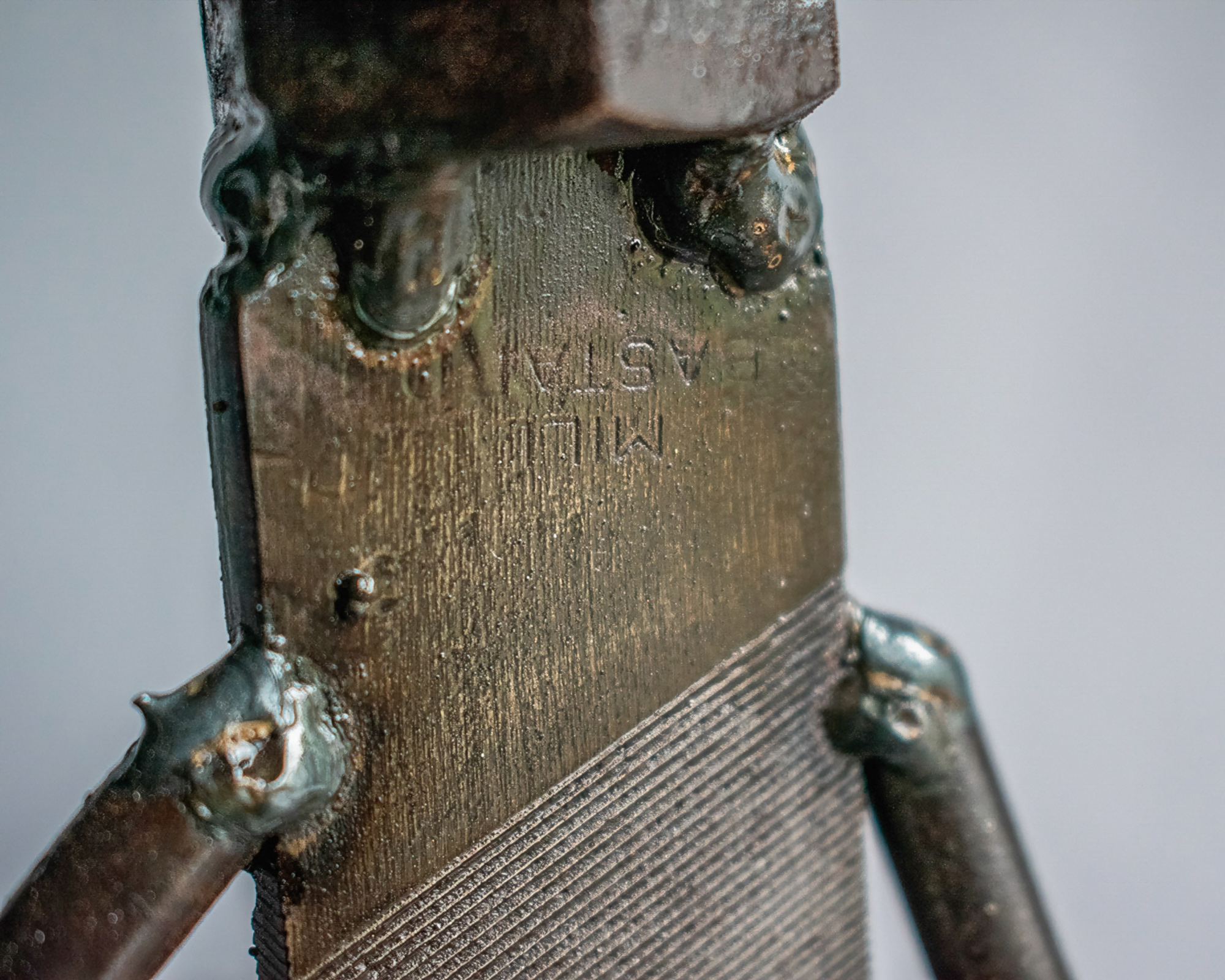Close-up of the metal file body, welds, and raw steel texture on a welded metal sculpture.
