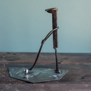 Welded metal golfer sculpture made from a railroad spike, square-head nails, and a ball bearing golf ball.