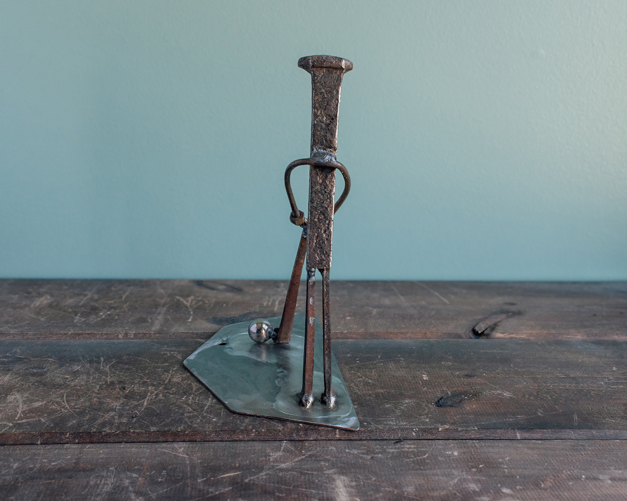 Back view of welded metal golfer sculpture on a raw steel base with a ball bearing golf ball.