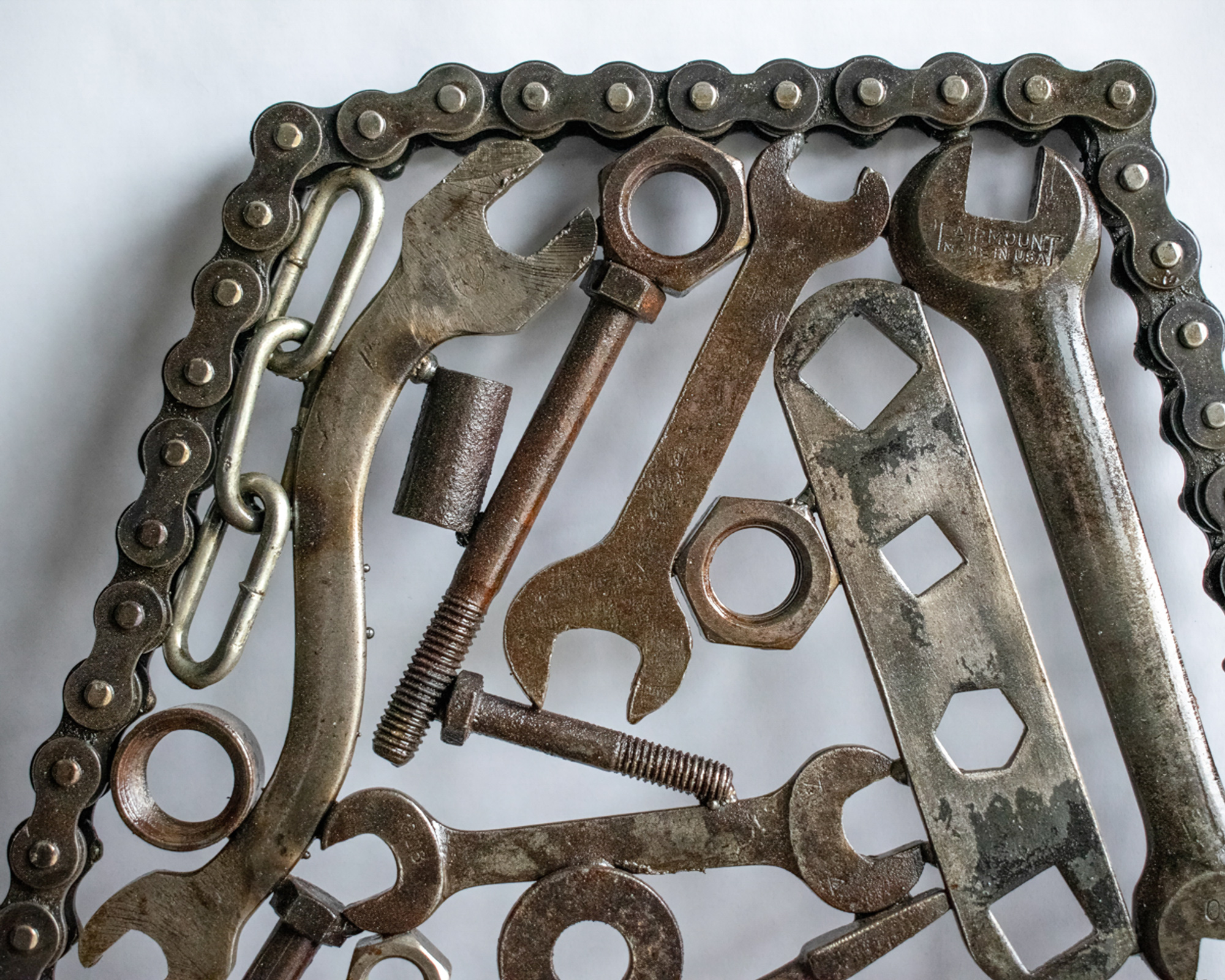 Close-up of welded tool sculpture with motorcycle chain frame, wrenches, bolts, and reclaimed metal parts.