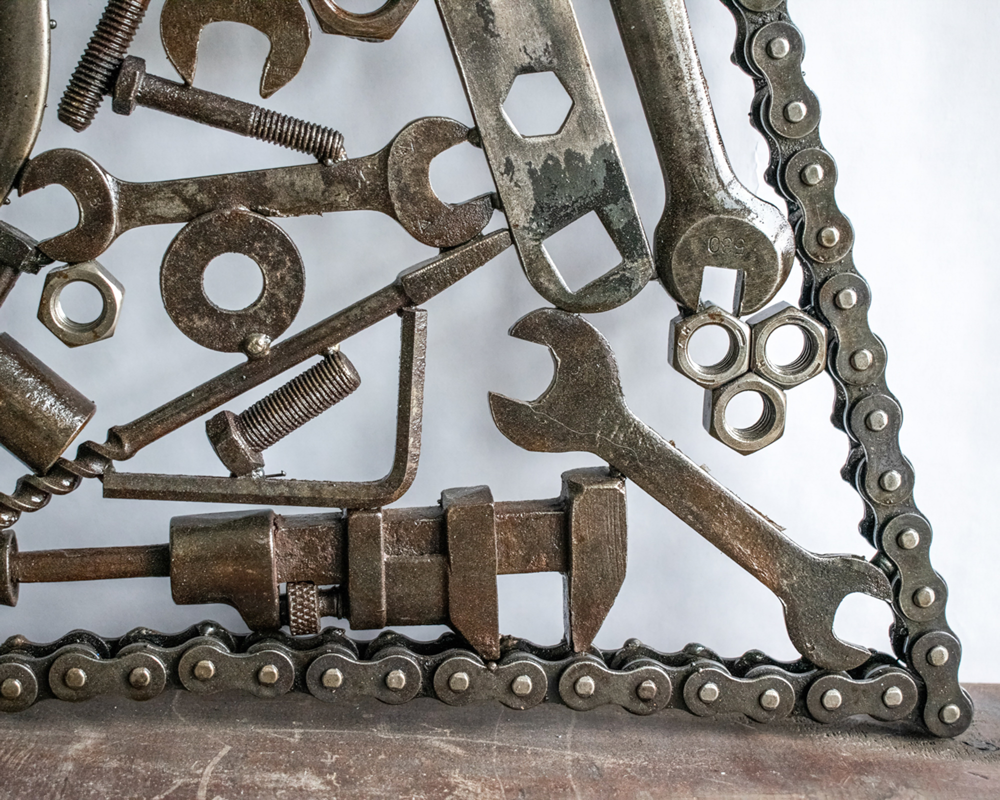 Close-up of reclaimed tool art showing wrenches, nuts, bolts, and motorcycle chain border.