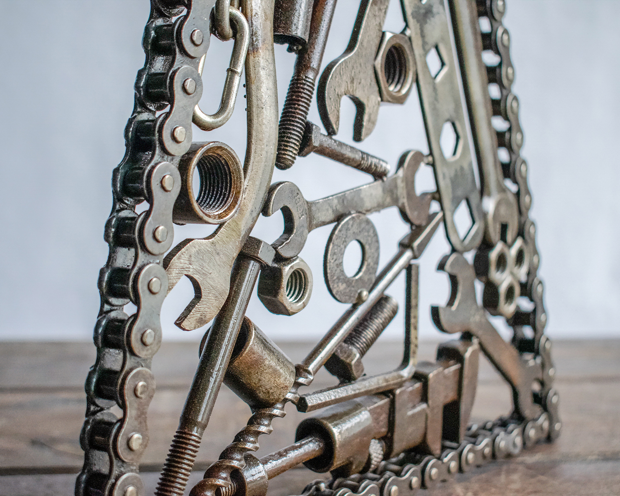 Angled view of industrial metal wall art made from welded tools and motorcycle chain.