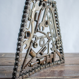 Side view of industrial metal wall art sculpture with layered wrenches, bolts, and motorcycle chain frame.