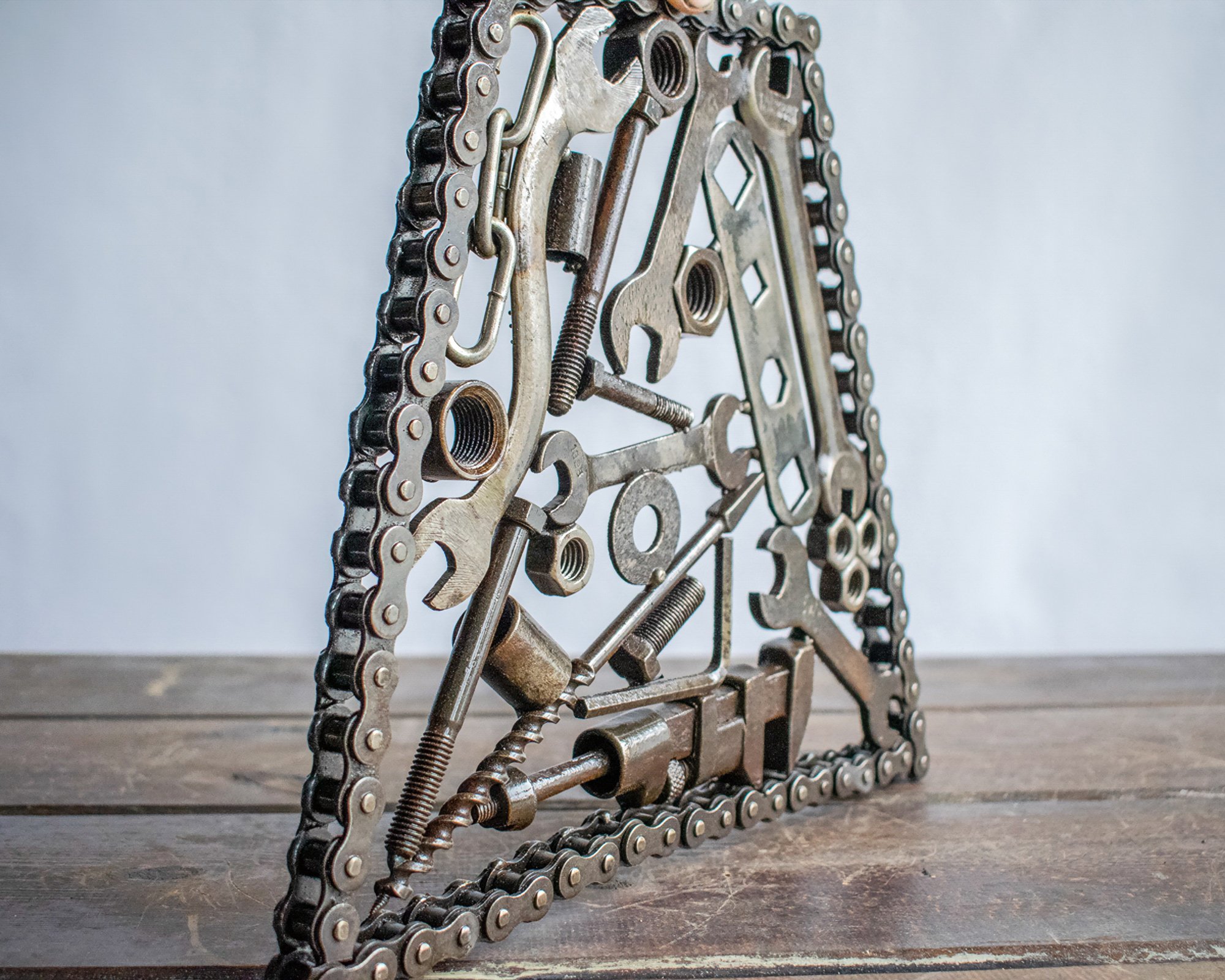 Side view of industrial metal wall art sculpture with layered wrenches, bolts, and motorcycle chain frame.