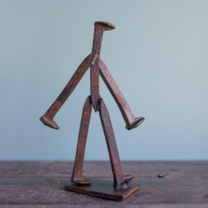 Angled view of handmade railroad spike art with a walking pose and raw steel finish.