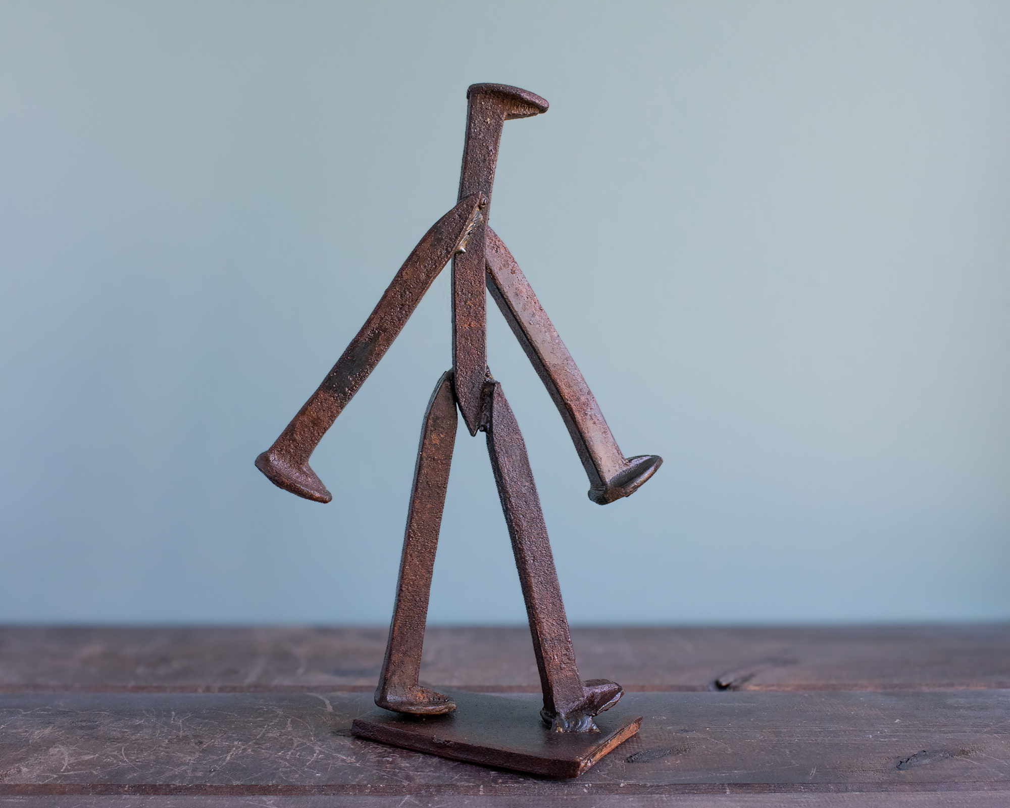 Angled view of handmade railroad spike art with a walking pose and raw steel finish.