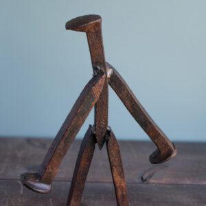 Close-up side view of welded railroad spikes forming the arms and body of a walking welded railroad spike sculpture.