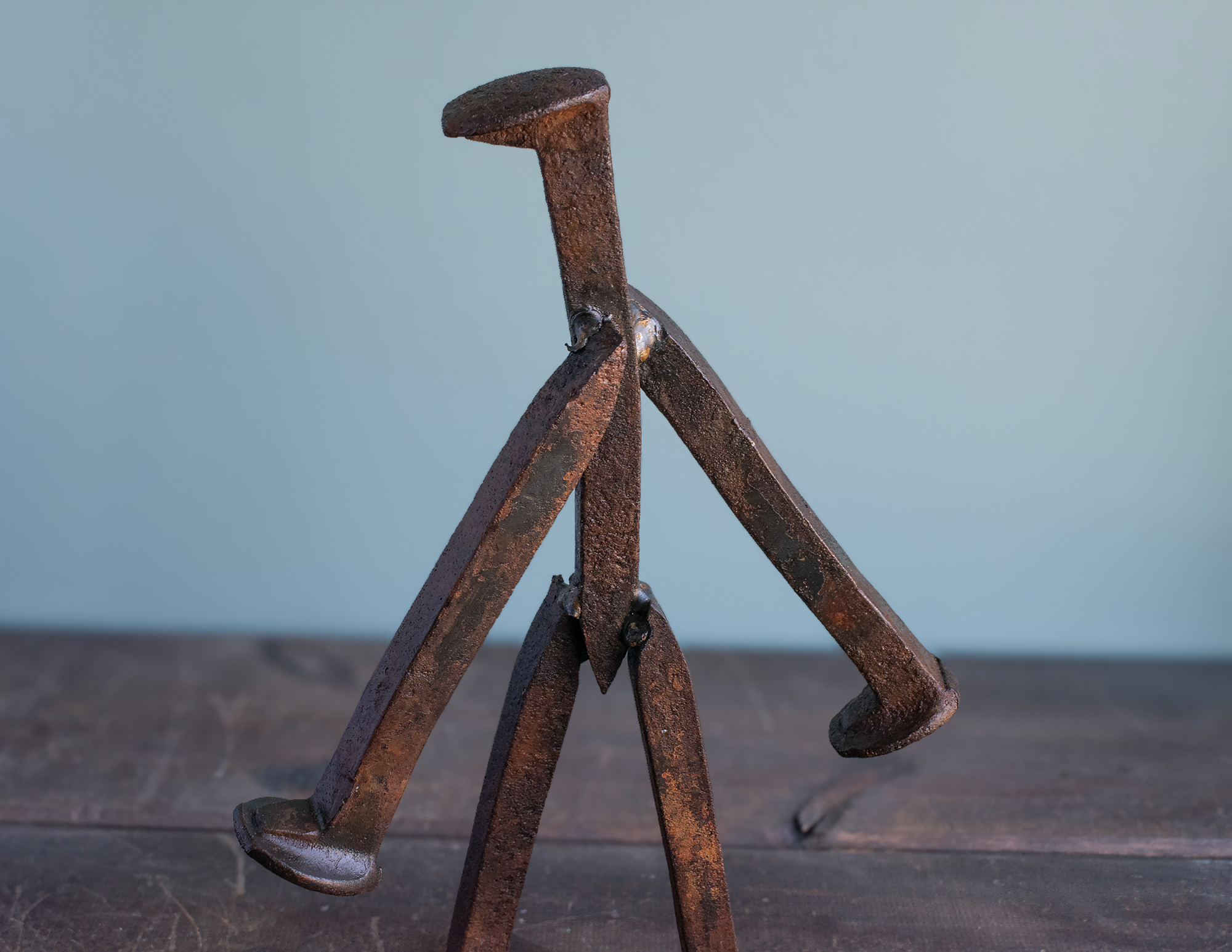 Close-up side view of welded railroad spikes forming the arms and body of a walking welded railroad spike sculpture.