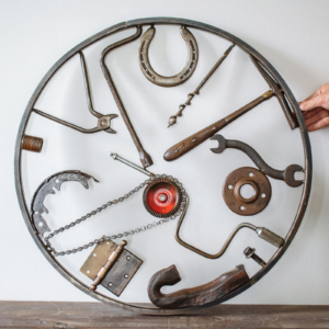 Welded metal wall art made from reclaimed tools, horseshoe, chain, hammer, and steel parts in a circular frame.