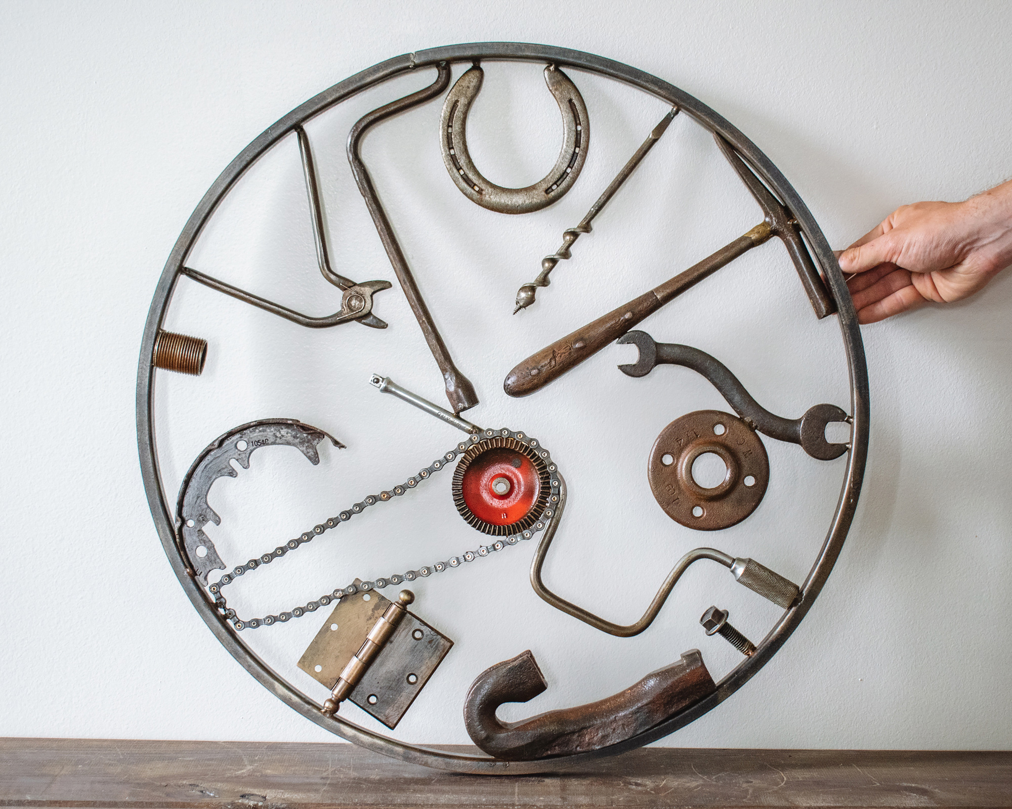 Welded metal wall art made from reclaimed tools, horseshoe, chain, hammer, and steel parts in a circular frame.
