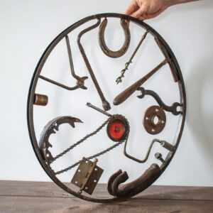 Industrial wall decor sculpture with reclaimed tools, horseshoe, chain, hammer, and circular steel frame.