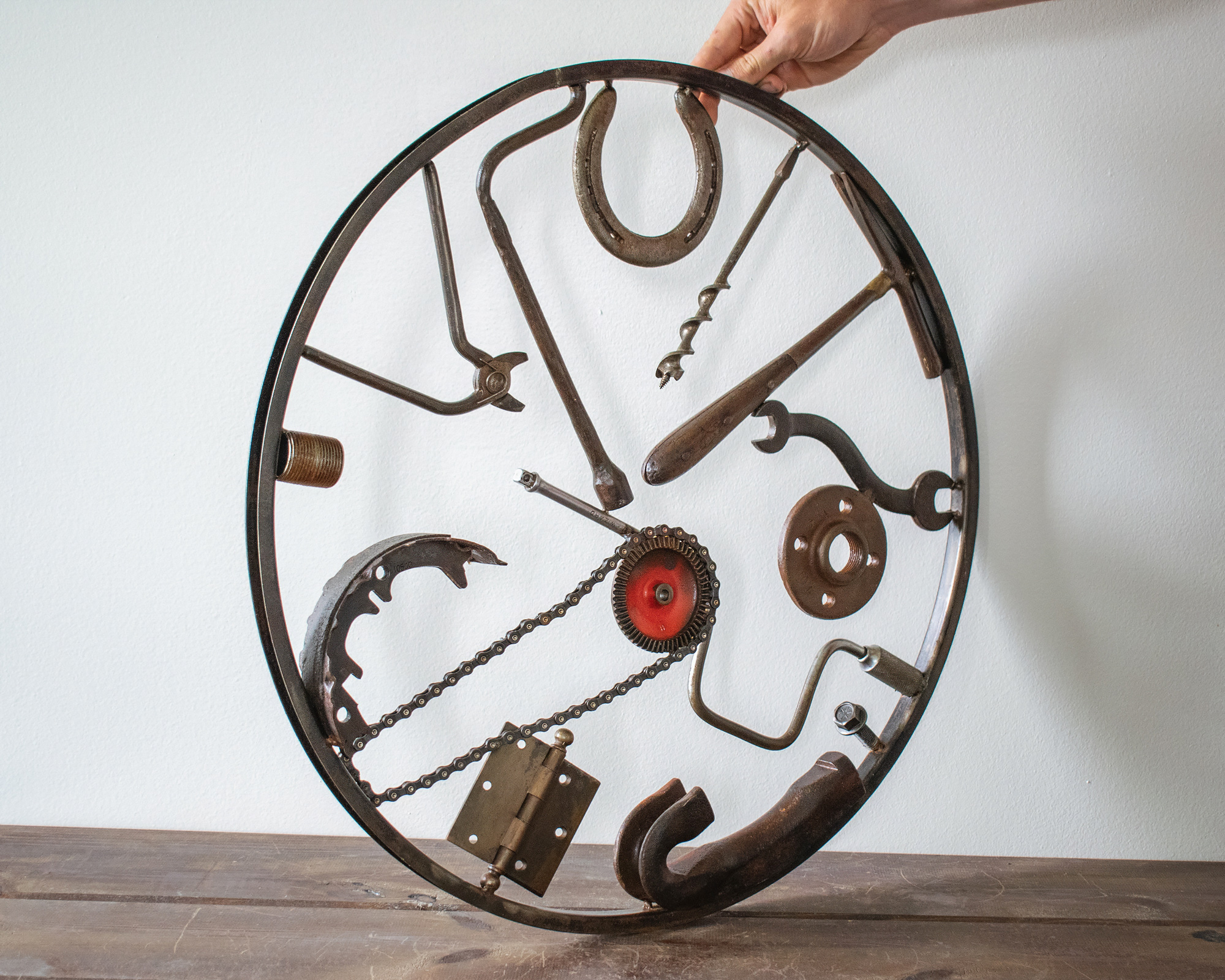 Industrial wall decor sculpture with reclaimed tools, horseshoe, chain, hammer, and circular steel frame.