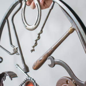Close-up of horseshoe, drill bit, hammer, and wrench details in a music-inspired wall art sculpture.