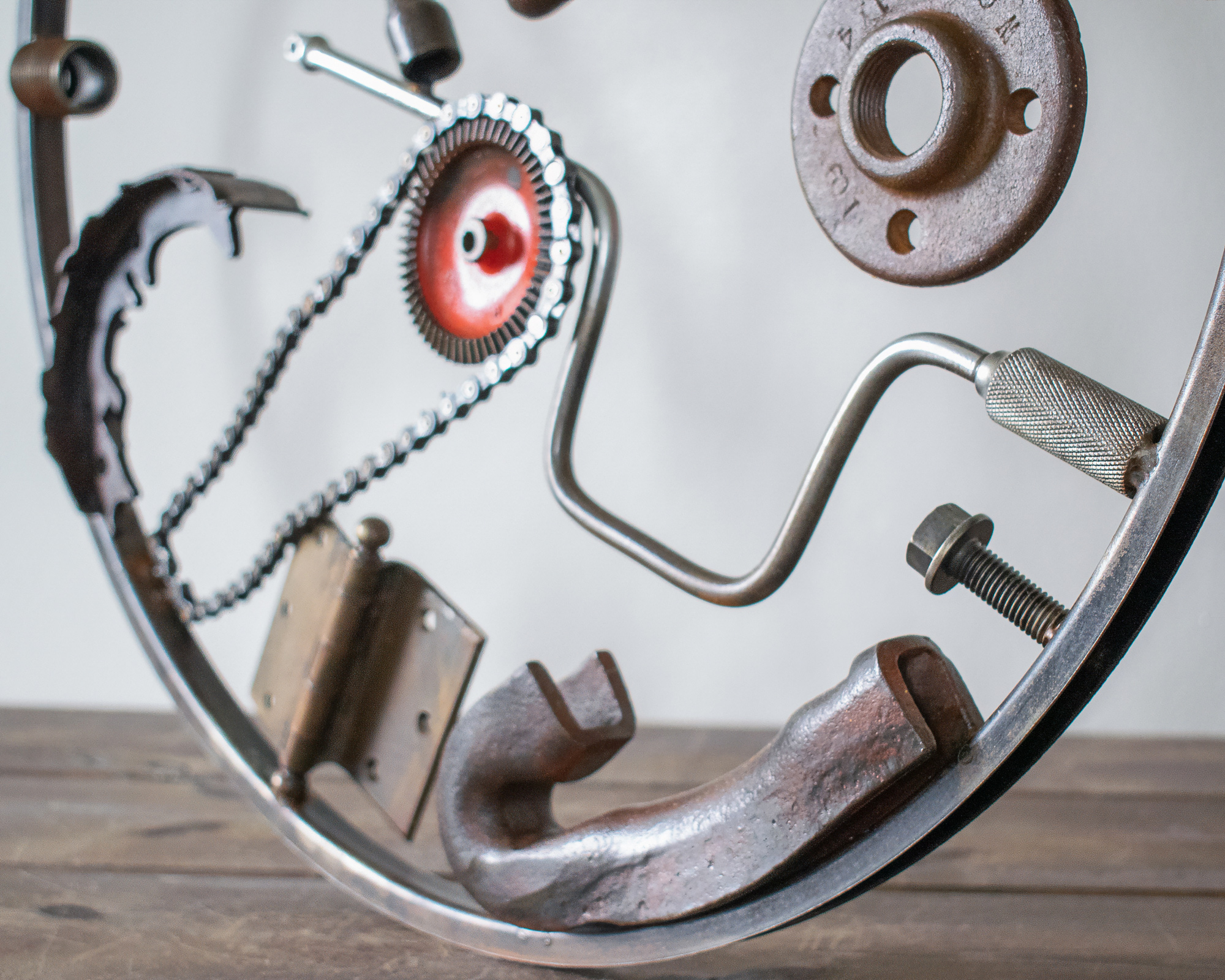 Close-up of reclaimed metal parts, chain, hinge, crank, and steel frame in a welded metal wall art collage.