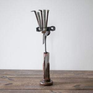 Back view of a welded scrap metal art sculpture showing the bolt base, steel body, and spring details.