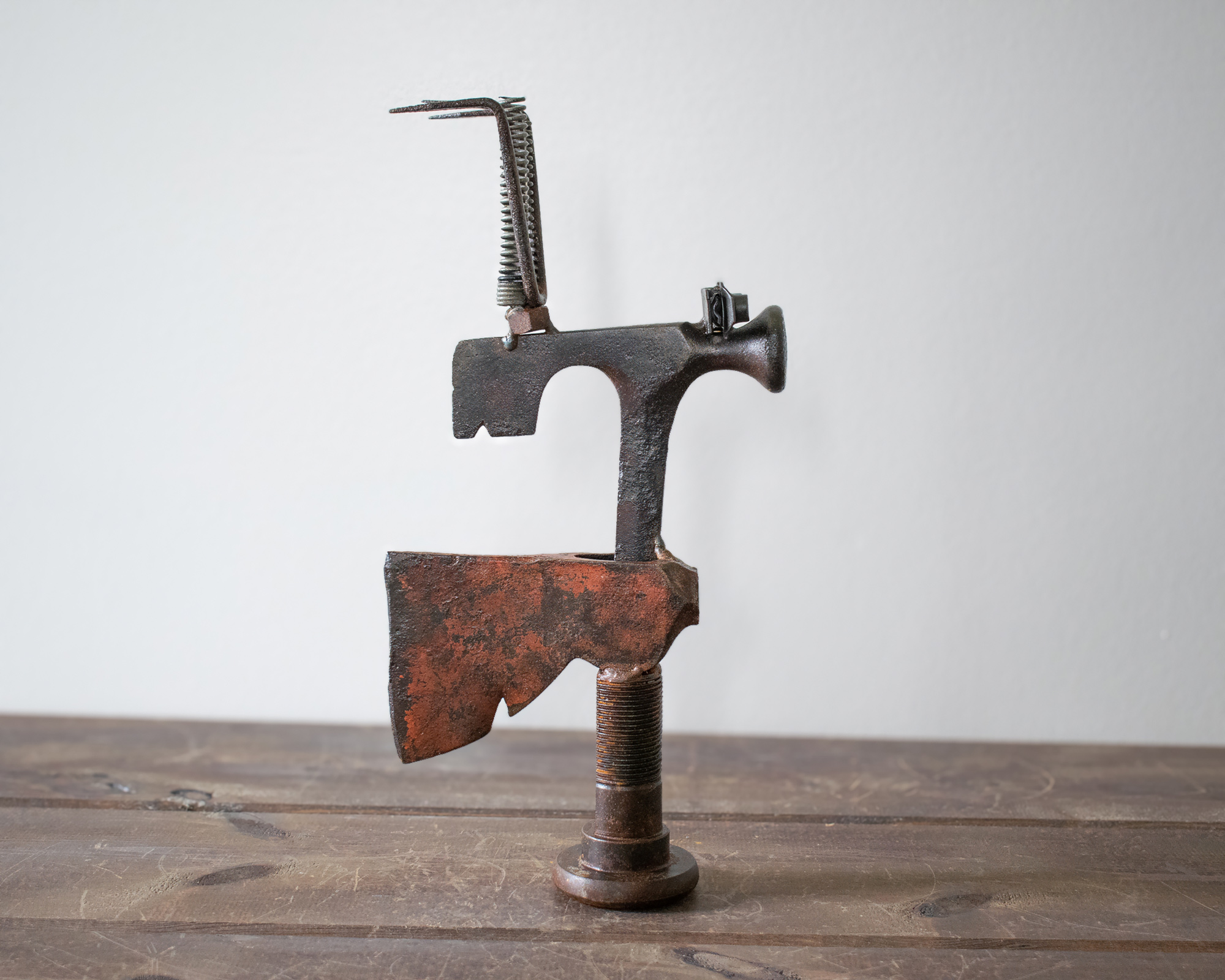 Side profile of a welded metal hatchet sculpture with a raw axe head, large bolt base, and garden rake detail.